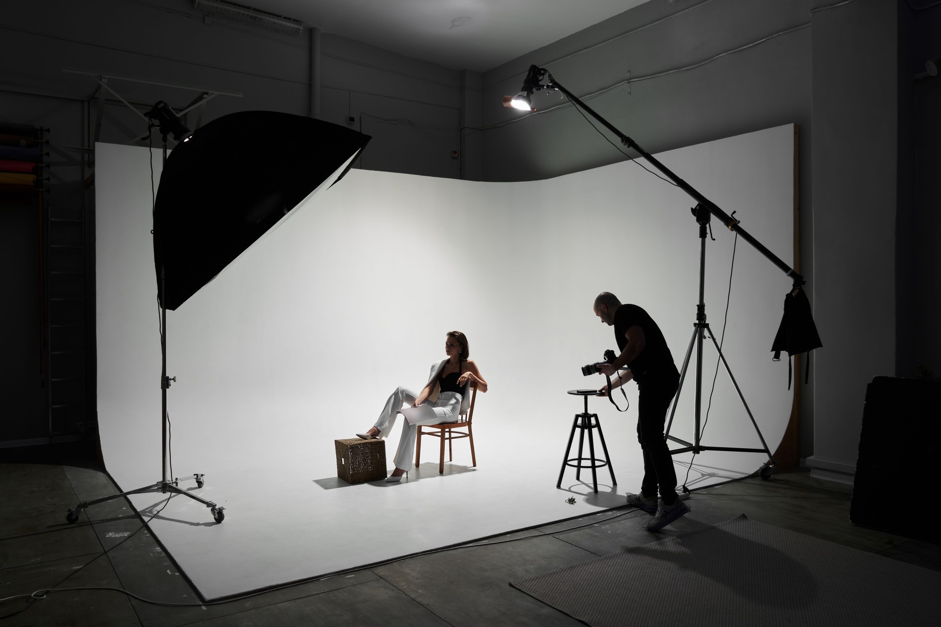 Fashion photography in a photo studio. Professional male photographer taking pictures of beautiful woman model on camera, backstage